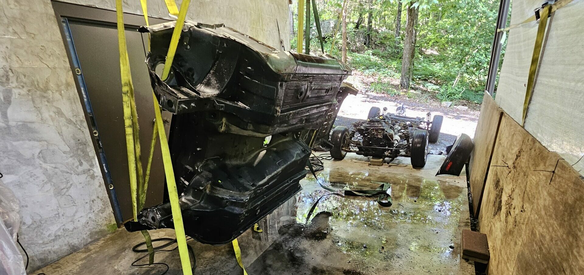 Pressure washed car chassis suspended in the air by tow straps for the exo car build. Lots of dirt and particulate on the floor.