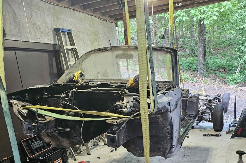 The Miata chassis lifted in the air with ratchet straps to remove the drivetrain and subframes as a single piece.