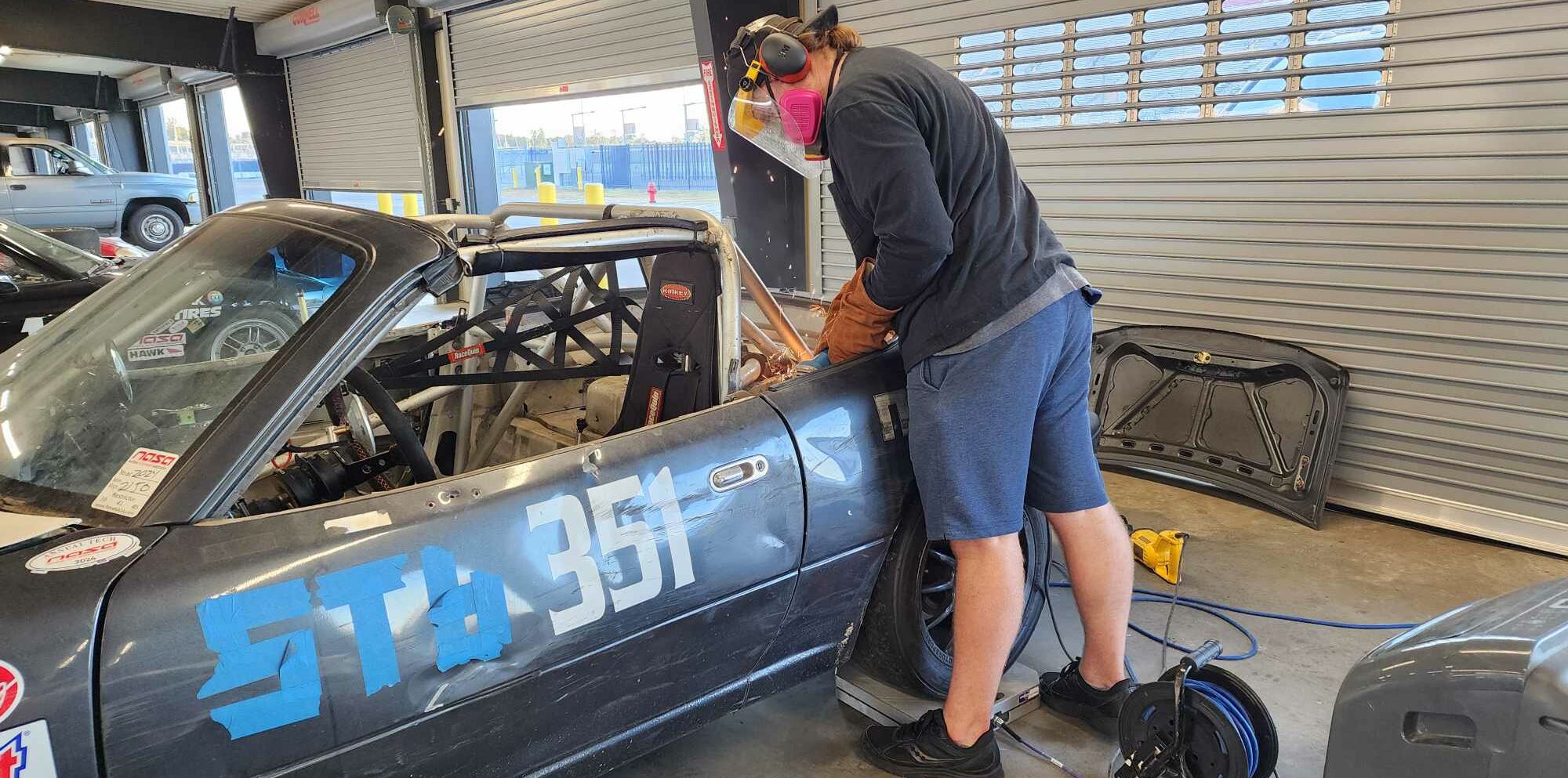 Suited up with safety gear cutting metal off the NA Miata Super Touring 6 Racecar.